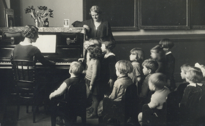 502152 Afbeelding van enkele kinderen van de Fröbelschool Ondiep 63 te Utrecht luisterend naar een leerkracht aan de piano.